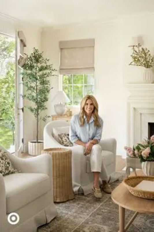 a woman sitting in a living room next to a fire place with flowers on the table