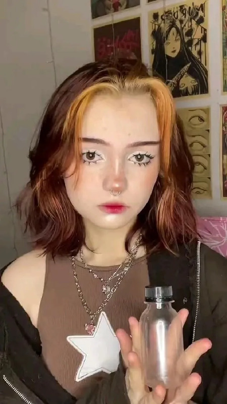 a girl with red hair holding a bottle in her hand and looking at the camera