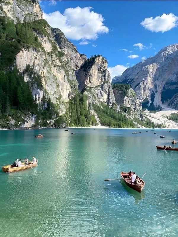 several small boats floating on top of a large body of water next to tall mountains
