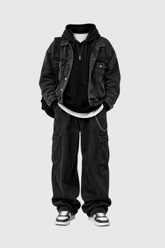 Minimal all black streetwear outfit featuring oversized denim jacket, black hoodie, baggy cargo pants and monochrome sneakers on a light grey background