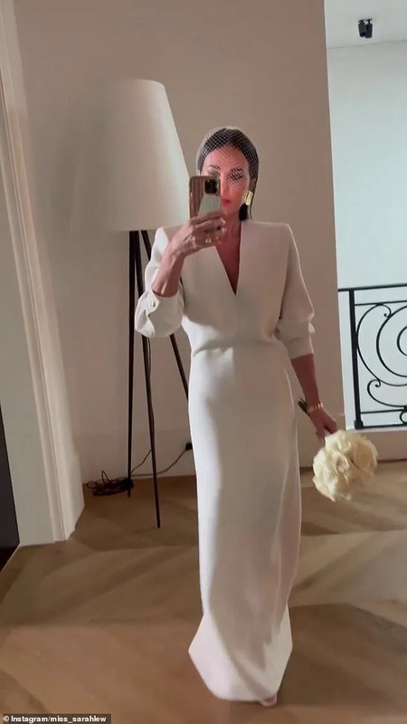 a woman in a white dress taking a selfie with her cell phone and holding a flower