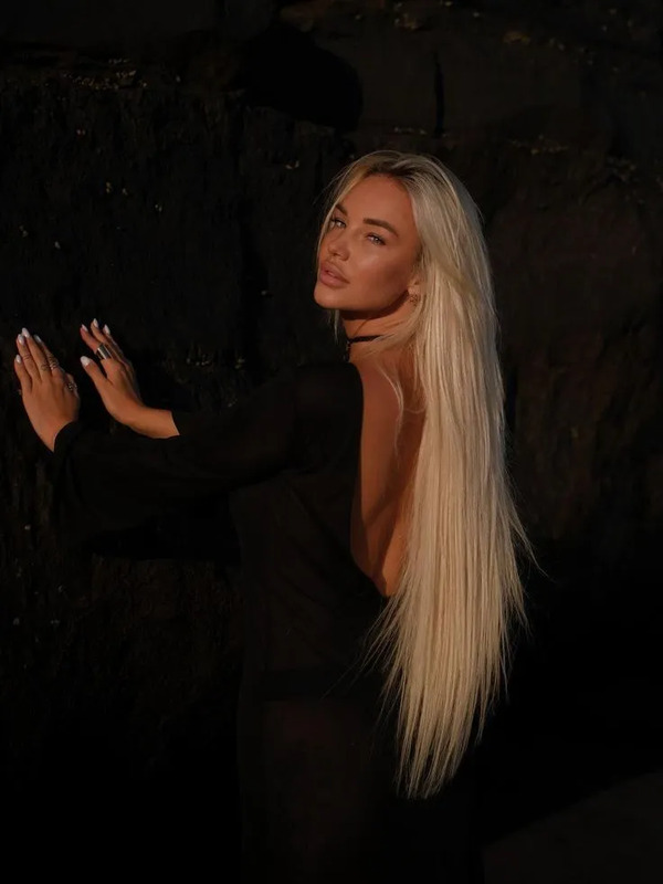 a woman with long blonde hair standing next to a rock