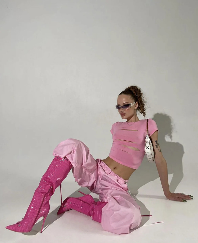 a woman sitting on the ground with her legs crossed and wearing bright pink pants, top and boots