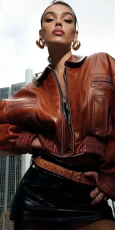 a woman wearing a brown leather jacket and black skirt