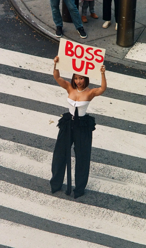 a woman holding up a sign that says boss up on the crosswalk at an intersection