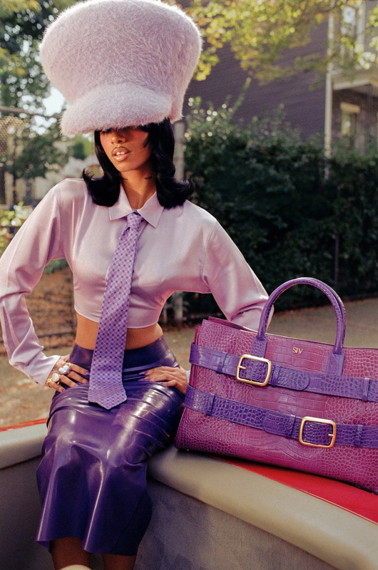 a woman sitting on the back of a truck wearing a hat and holding a purple purse