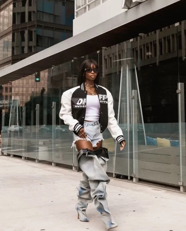 a woman is walking down the street in ripped jeans and a white jacket with black lettering on it