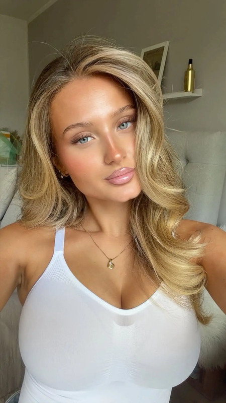 a woman with blonde hair wearing a white top and posing for the camera in front of a mirror