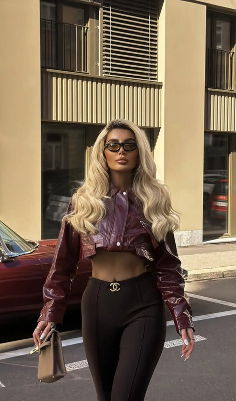 a woman walking down the street wearing black pants and a cropped top with leather sleeves