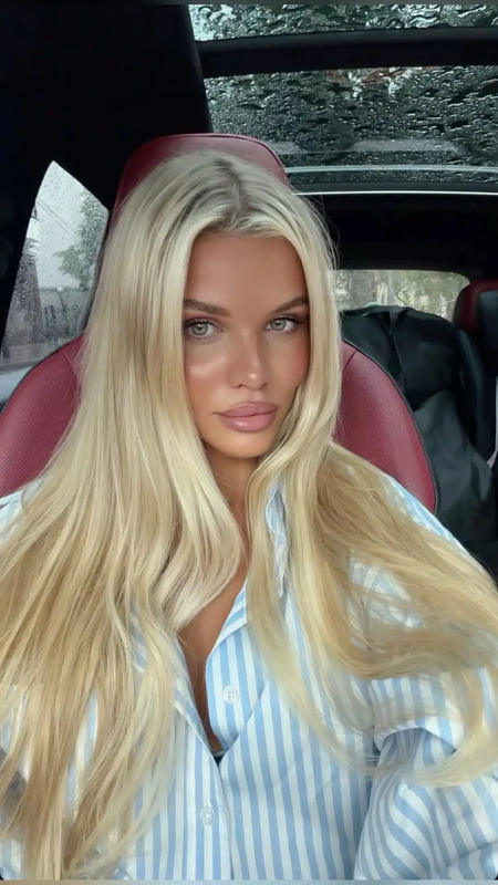a woman sitting in the back seat of a car with long blonde hair and blue eyes