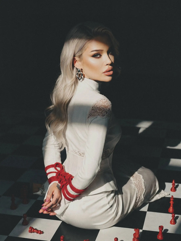 a woman sitting on top of a black and white checkered floor next to chess pieces