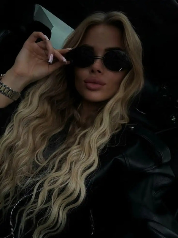 a woman with long blonde hair and black sunglasses is sitting in the back seat of a car