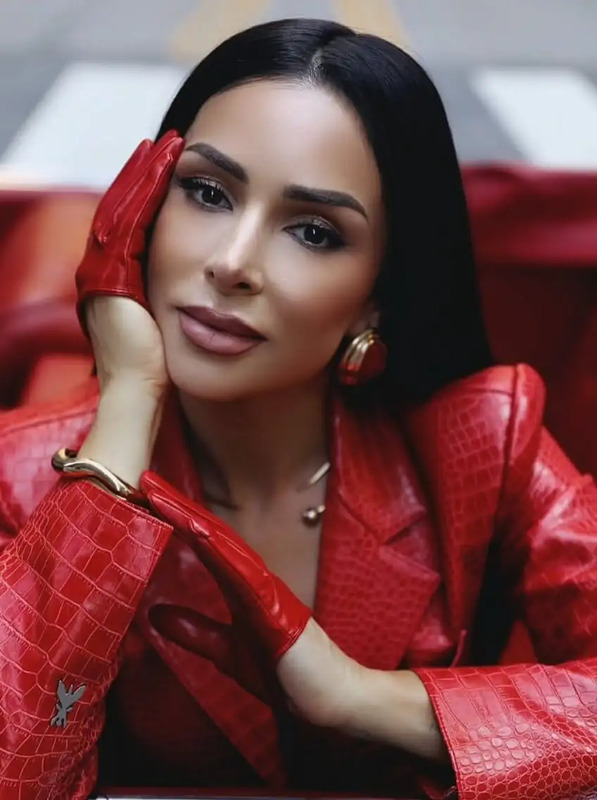 a woman in a red leather jacket and gold earrings posing for the camera with her hand on her face