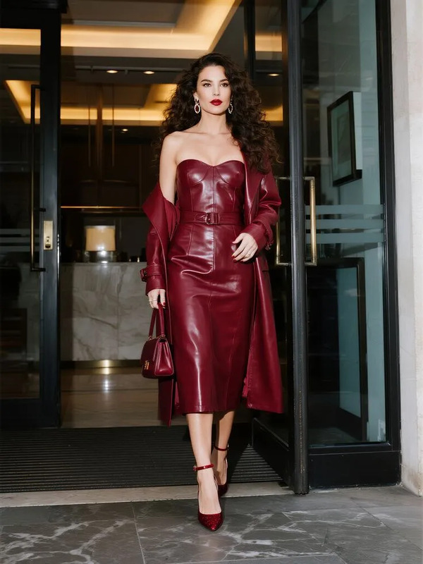 a woman in a red leather dress is walking out of a building with her hand on her hip