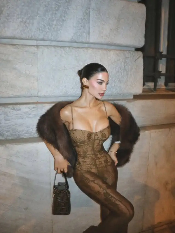 a woman standing next to a stone wall with a fur stole around her neck and handbag