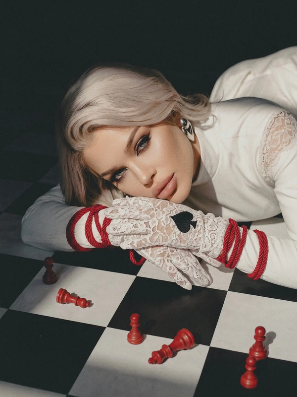 a woman laying on top of a checkered floor next to red and white chess pieces
