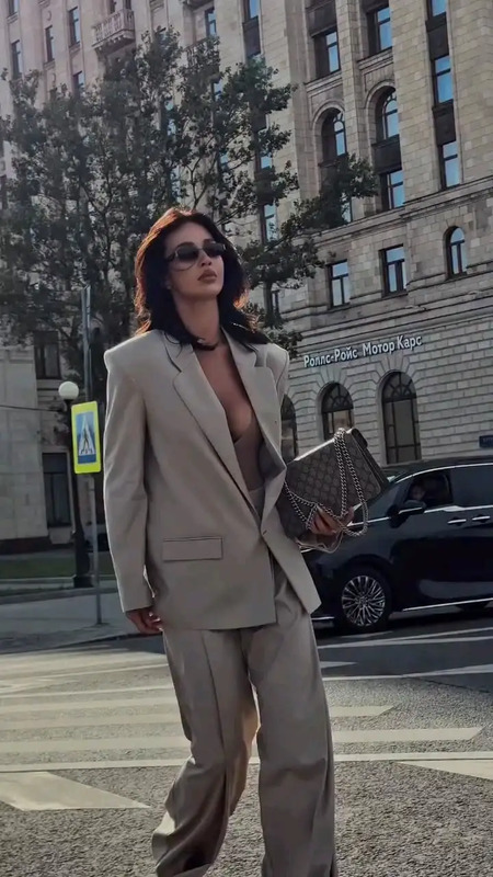 a woman in a tan suit and sunglasses walking across the street with her handbag