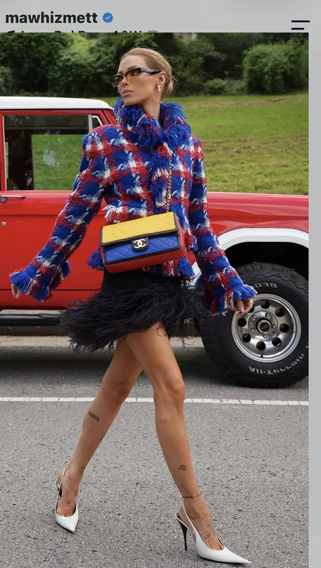 a woman walking down the street carrying a blue and yellow bag with feathers on it