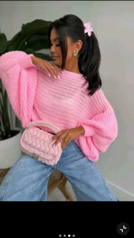 a woman in pink sweater and jeans sitting on a chair holding a pink handbag