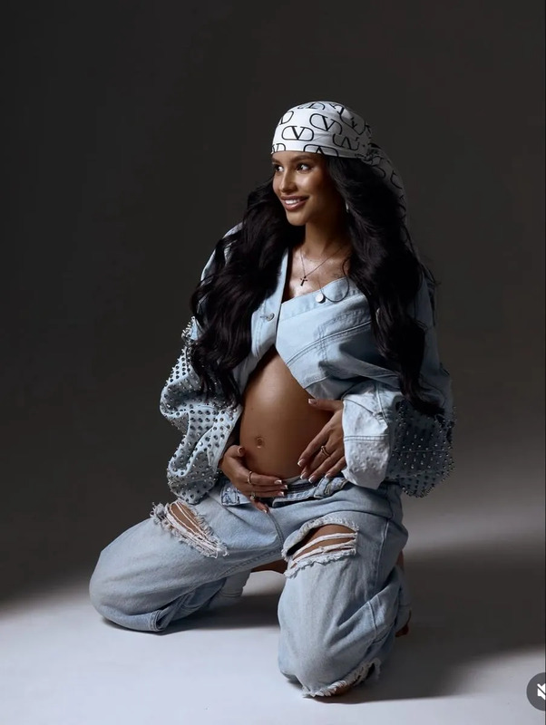 a pregnant woman sitting on the ground wearing ripped jeans and a headband, with her belly exposed