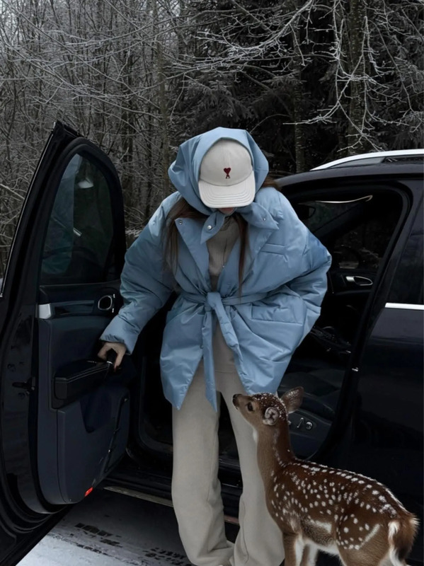 a woman standing next to a car with a deer in the door and wearing a hat