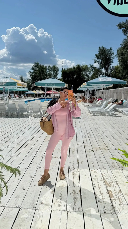 a woman taking a selfie in front of a pool with chairs and umbrellas