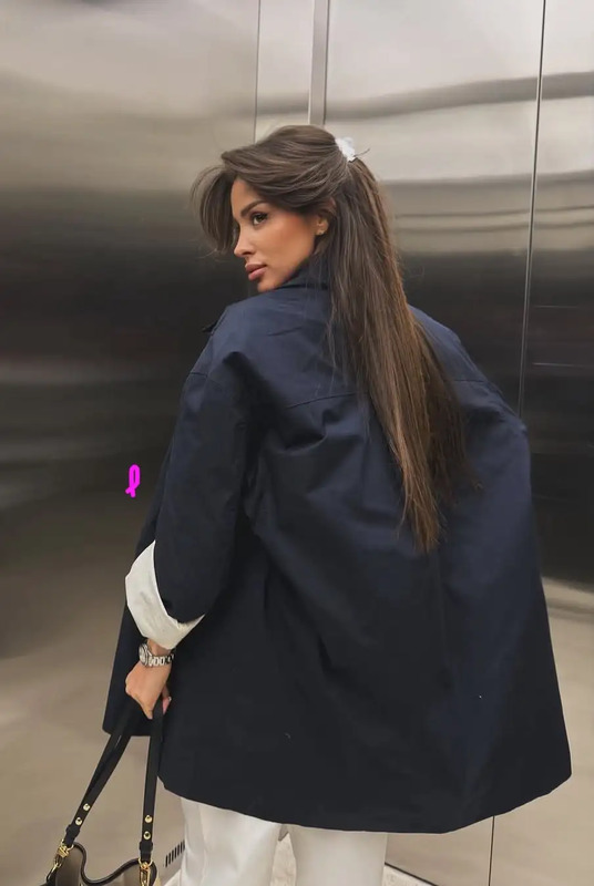 a woman in white pants and a blue jacket carrying a black handbag while standing next to an elevator