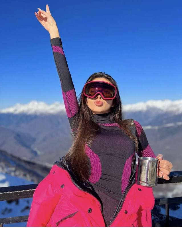 a woman wearing ski goggles and holding her arms in the air
