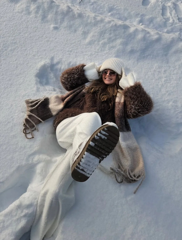 a woman is laying in the snow with her feet up and wearing winter clothing on