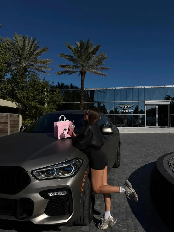 a woman leaning on the hood of a car with a shopping bag in her hand