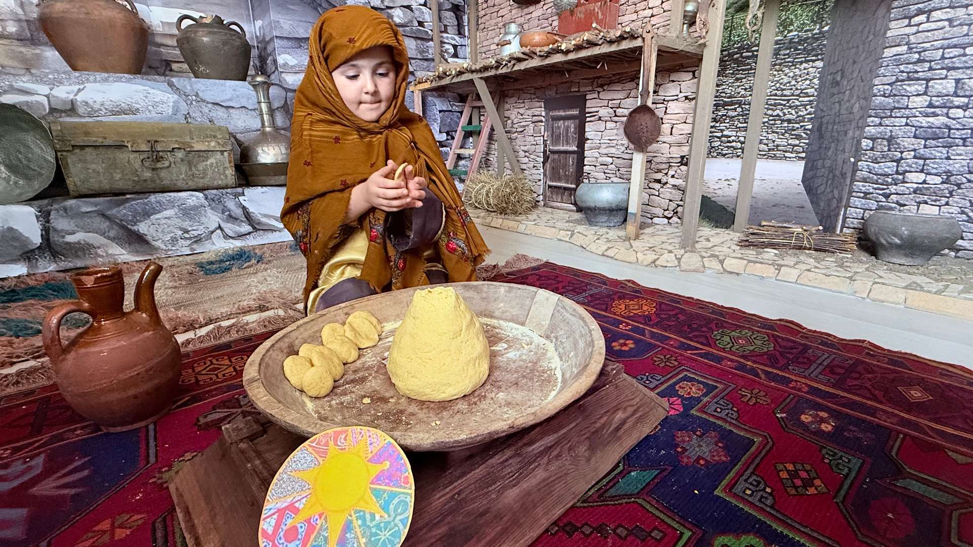 На кадре запечатлена сцена
«Хранительница очага». Девочка в национальном костюме играет роль хозяйки дома, готовящей хинкал. Её образ и окружение создают атмосферу традиционного горского быта. Ведь наши бабушки месили самое вкусное тесто. Каждая семья имеет свой секрет его приготовления, хинкал — это не просто еда, это целый ритуал, который подчёркивает сакральную ценность этого обычая как основы семейной жизни.
