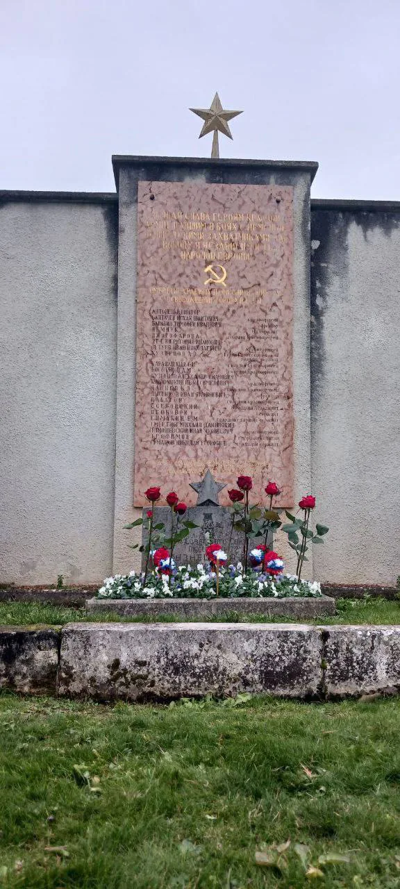Мемориальная плита с именами павших, цветы у надгробия