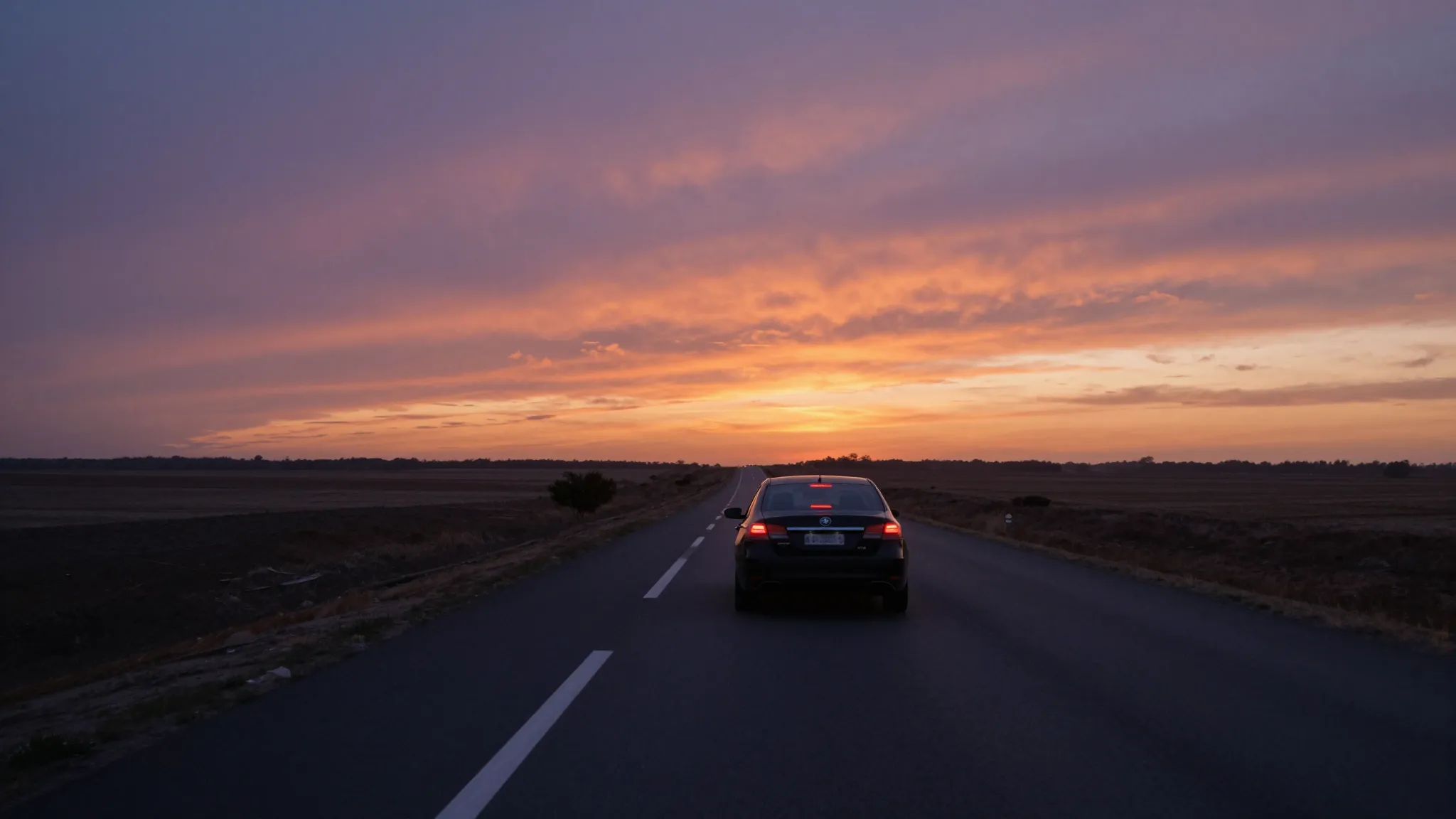A black car driving away on a lonely highway towards the hor...