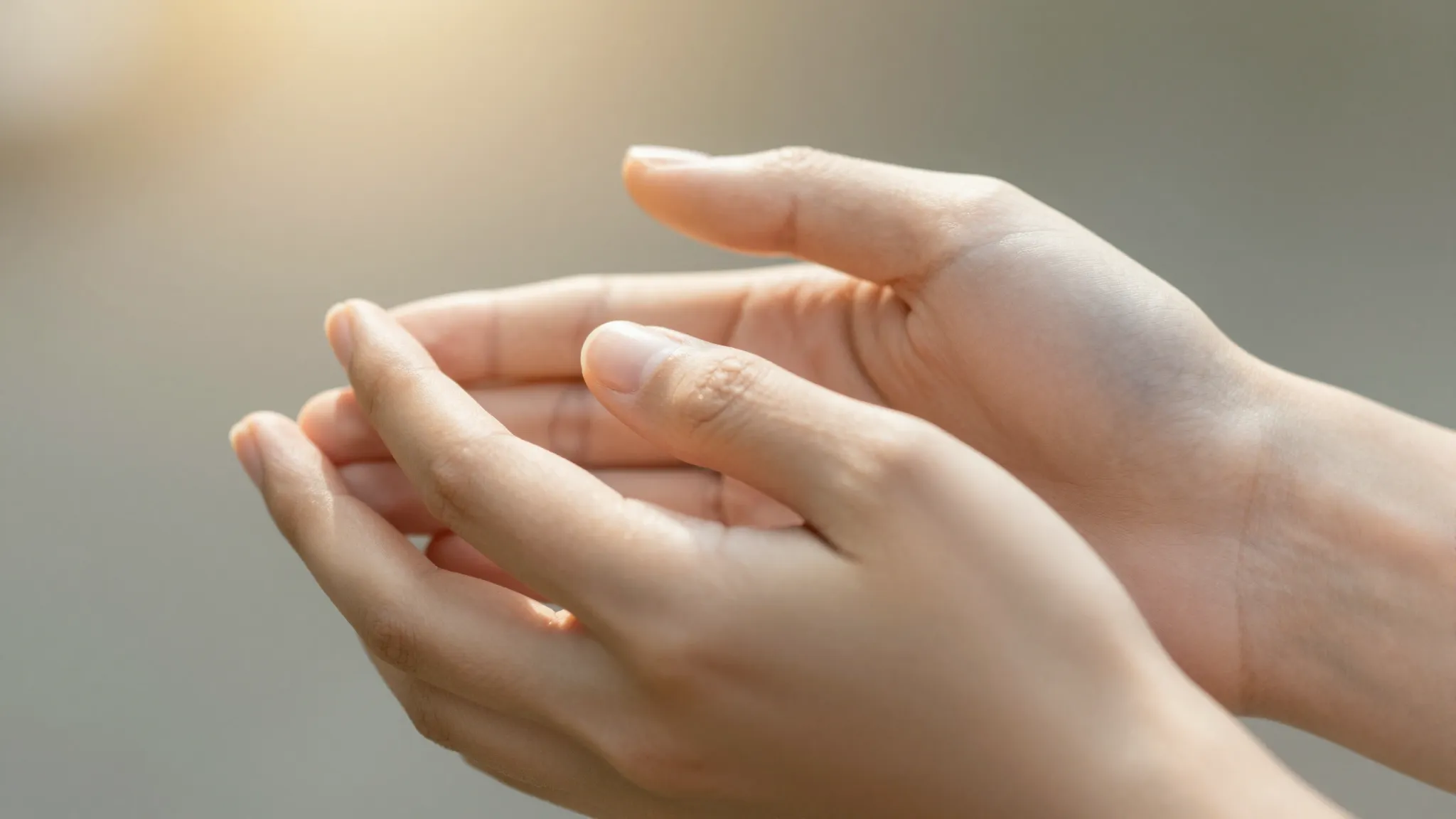 Two hands holding each other gently, warm sunlight filtering...