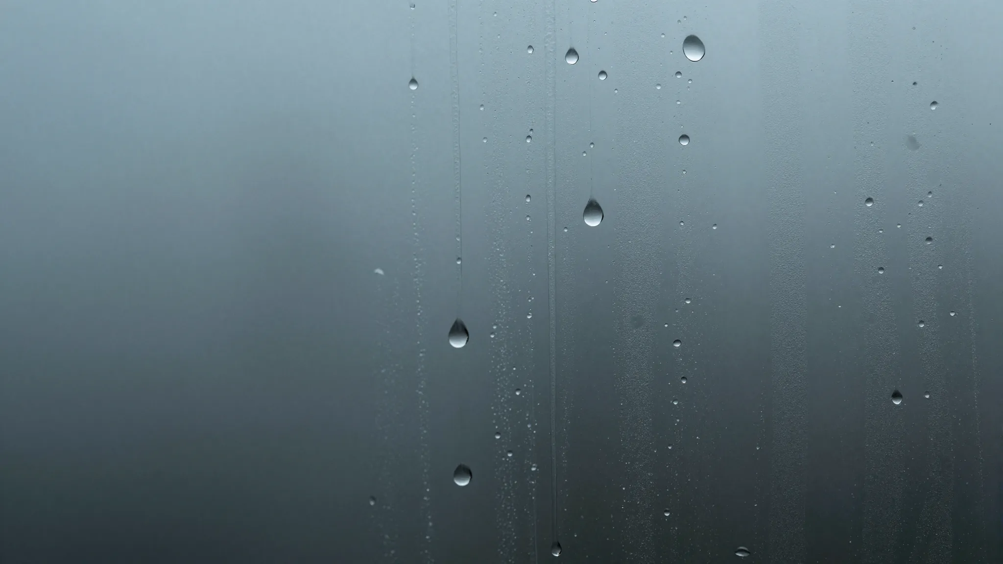 Macro shot of heavy water droplets on glass, merging into lo...