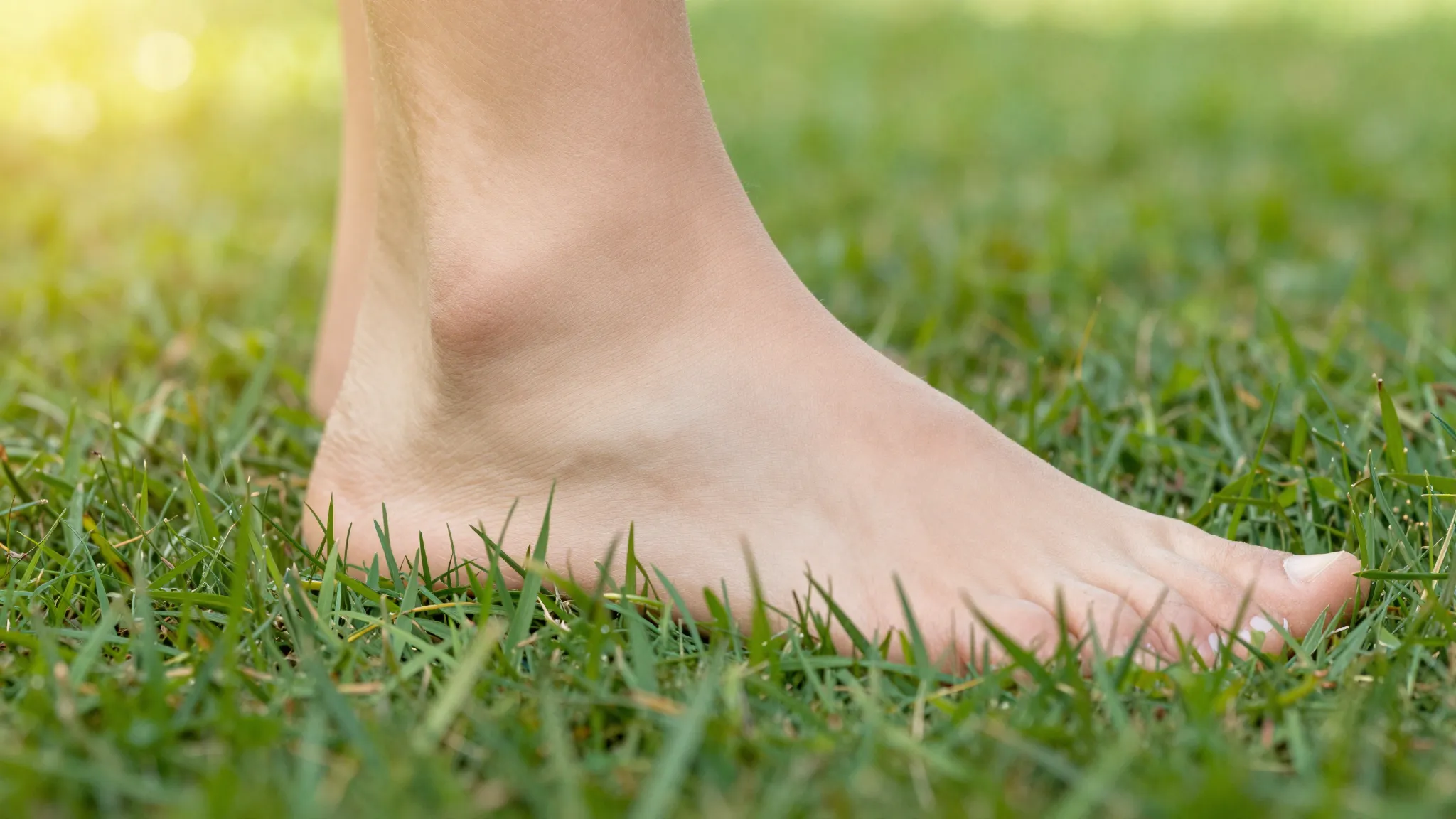 Close-up of a healthy foot stepping on green grass, sunlight...