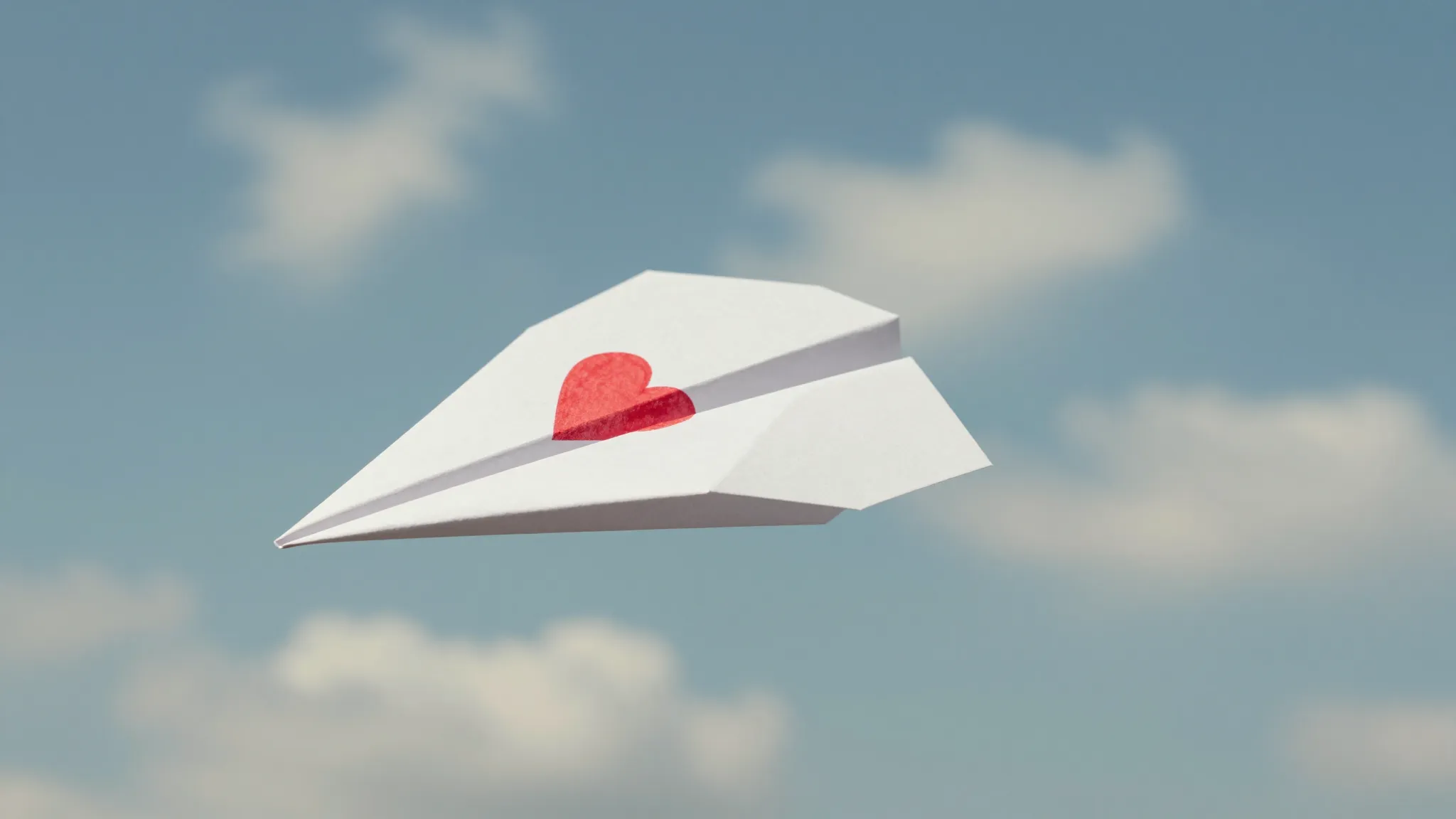 A delicate paper airplane flying through a soft blue sky wit...