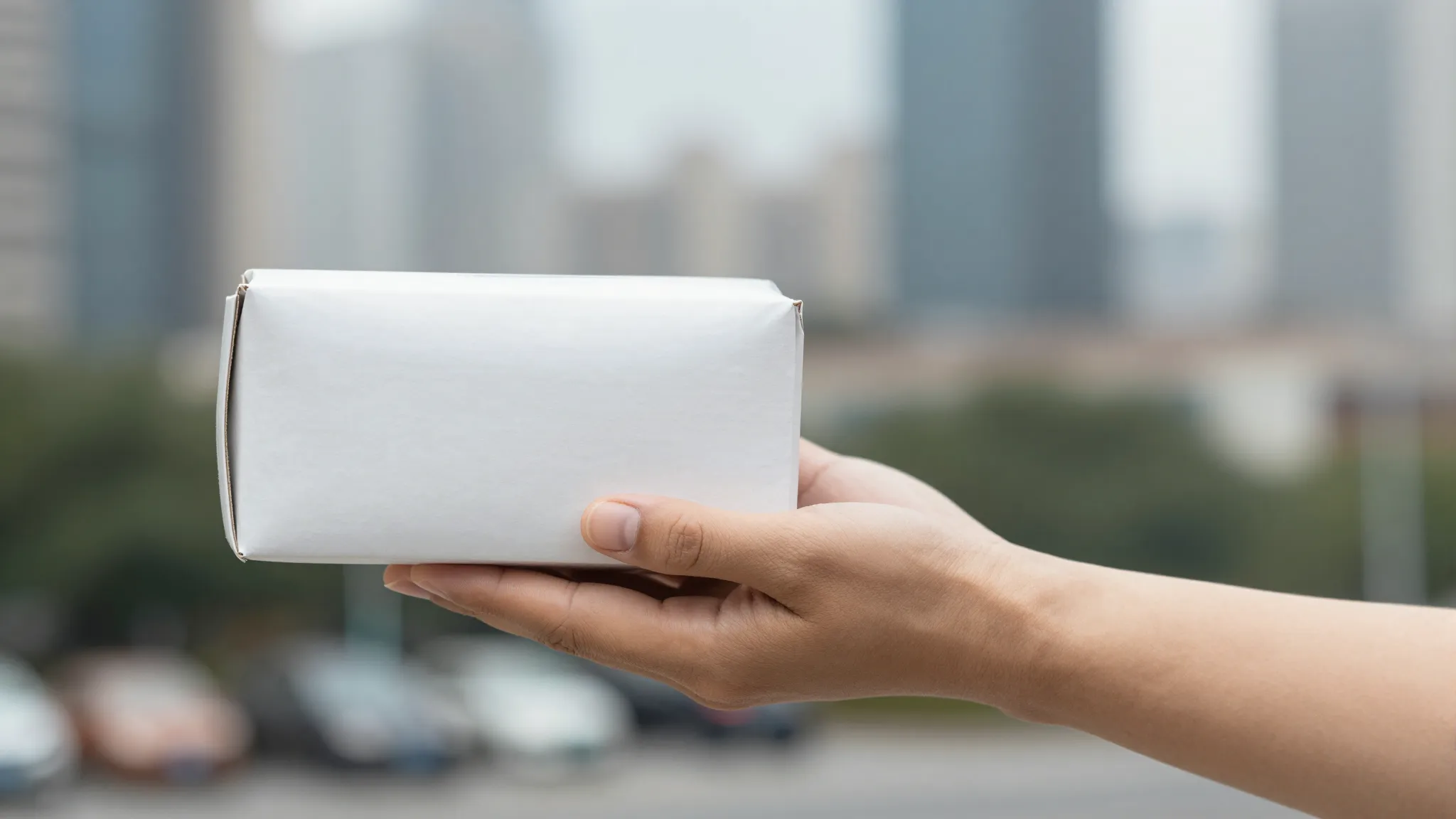 A delivery courier hand holding a small white package, blurr...
