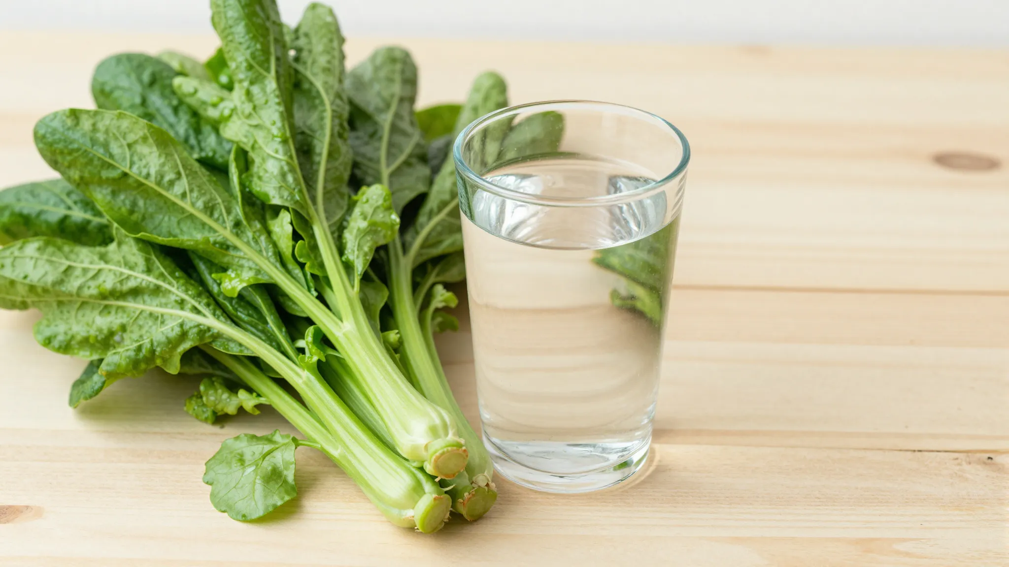 Fresh green vegetables and a glass of clean water on a woode...
