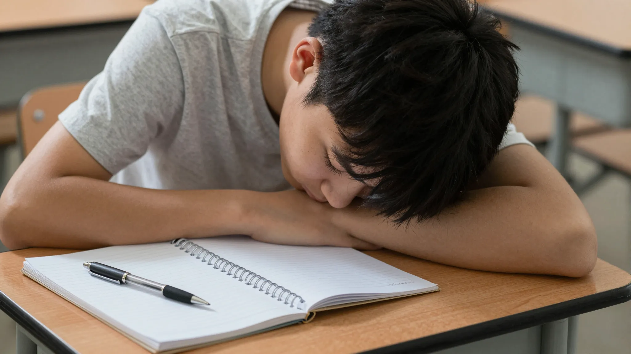 Close-up of a teenager with his head down on a school desk. ...