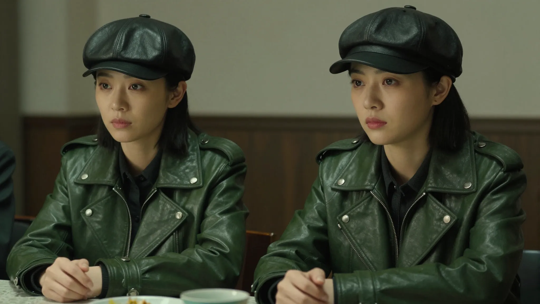 Two serious Chinese women sitting at a table, wearing green ...