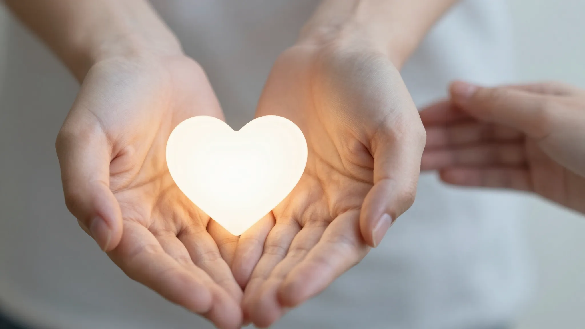A pair of hands holding a small glowing heart, soft natural ...