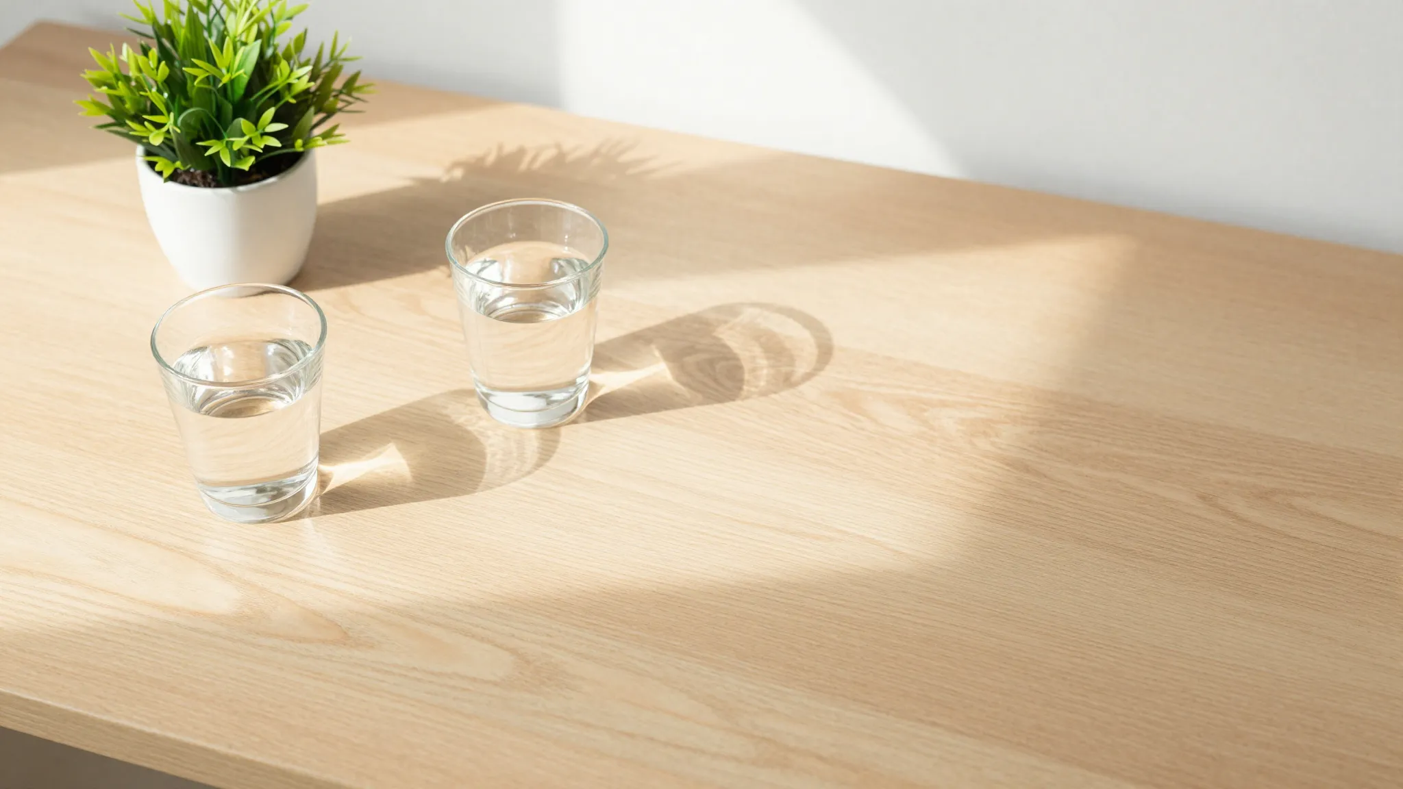 A minimalist workspace with a wooden desk, a glass of water,...