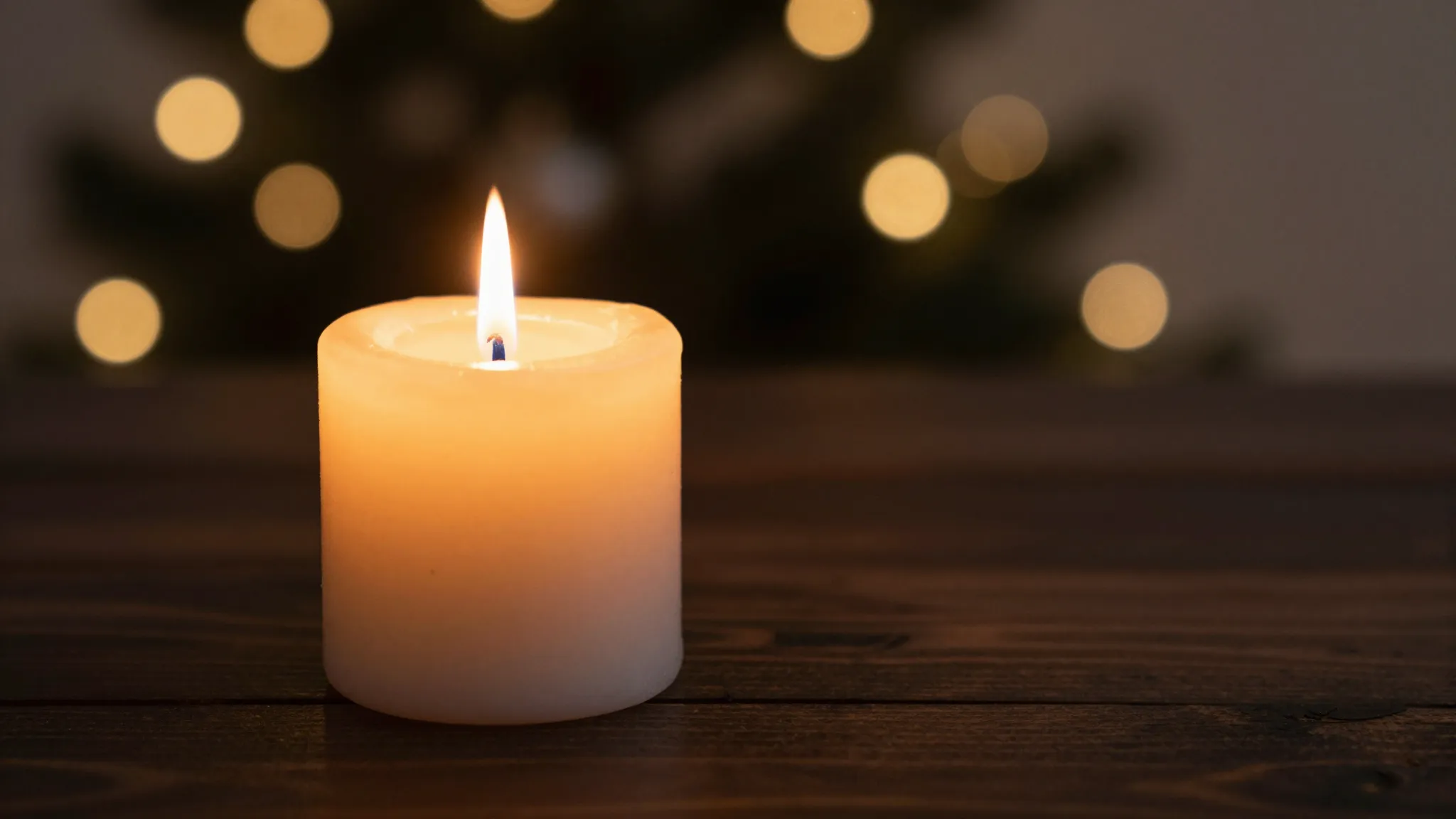 Close-up of a single burning candle on a dark wooden surface...