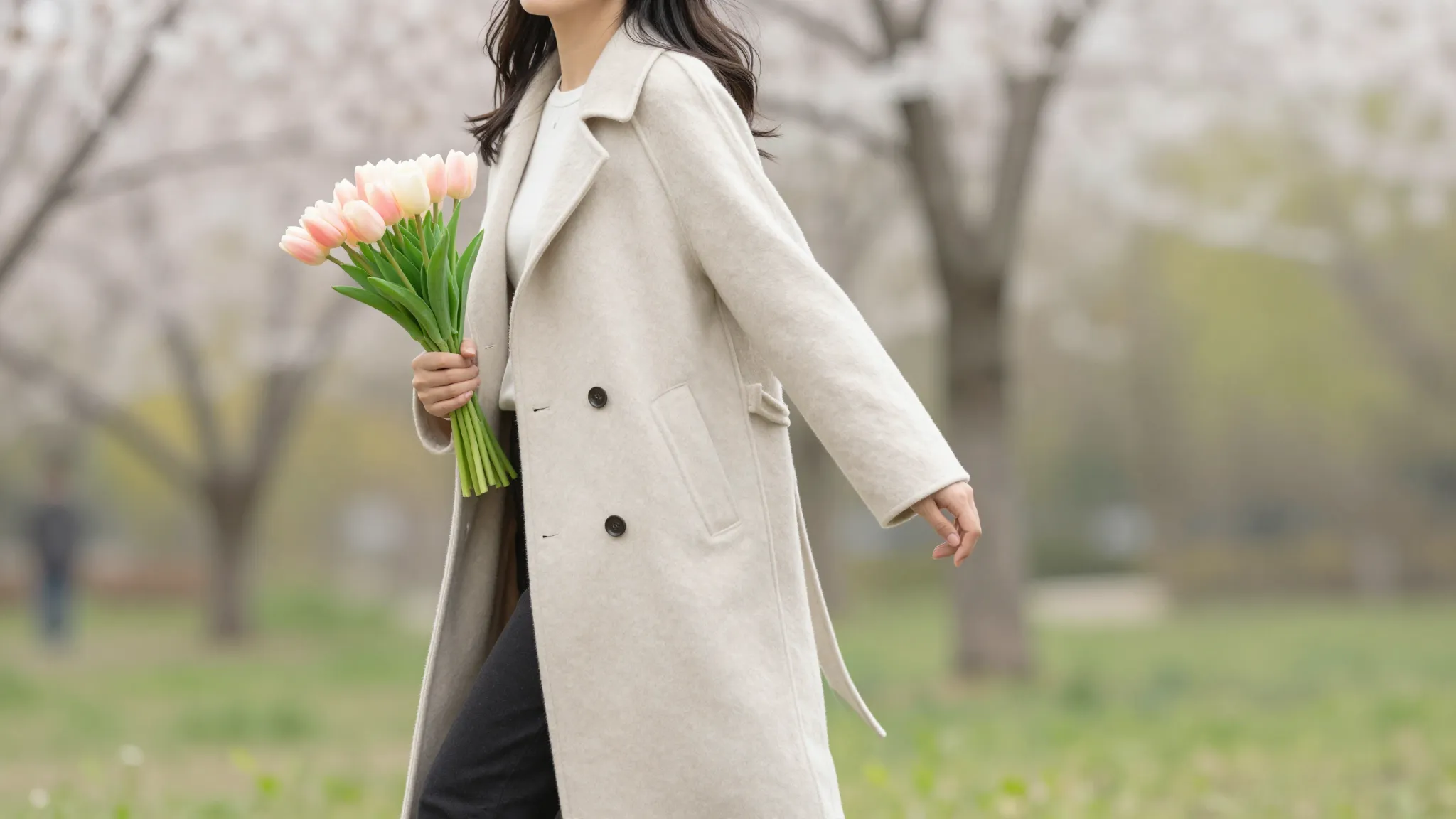 A stylish woman in a light beige coat holding a bouquet of t...