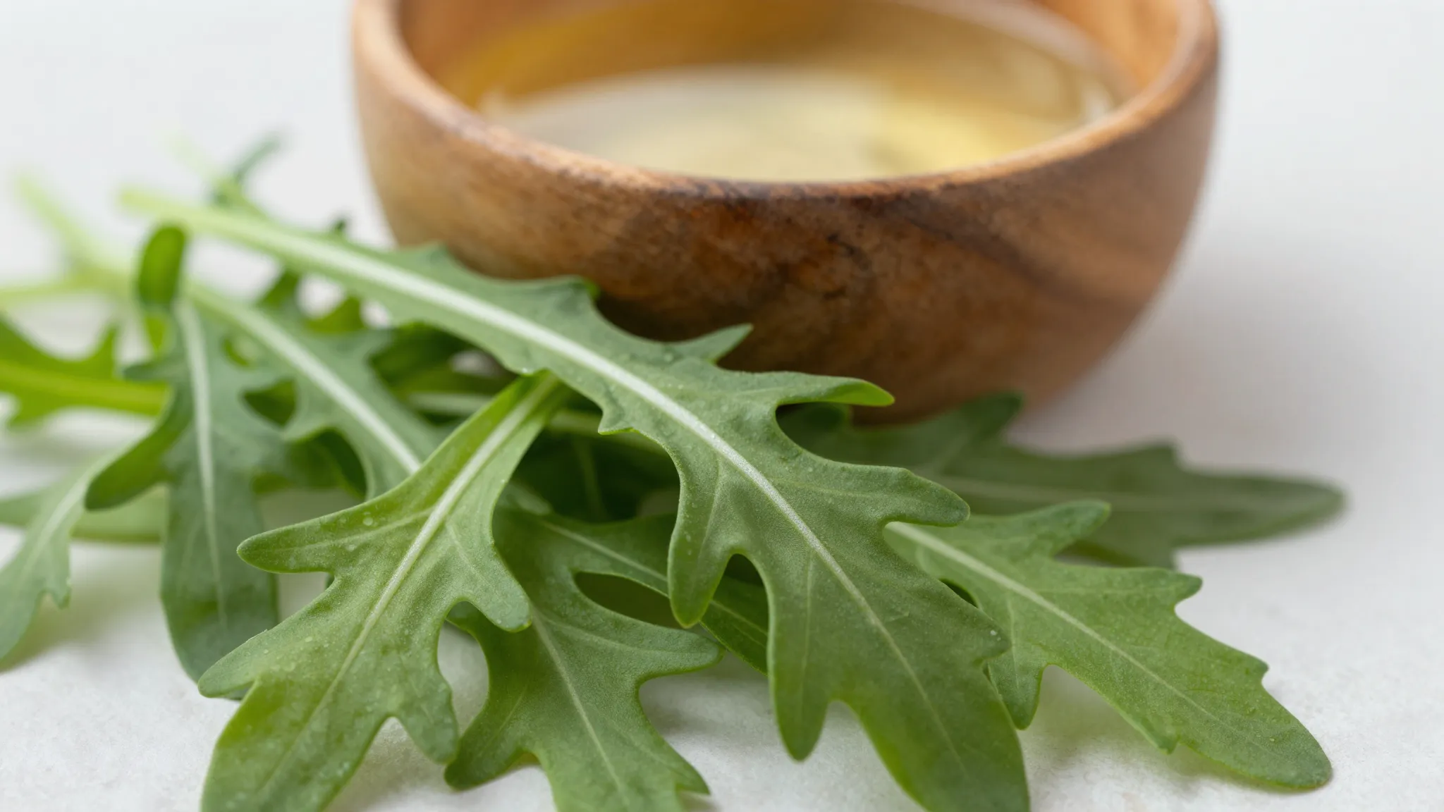 Close-up of fresh green arugula leaves and a small wooden bo...