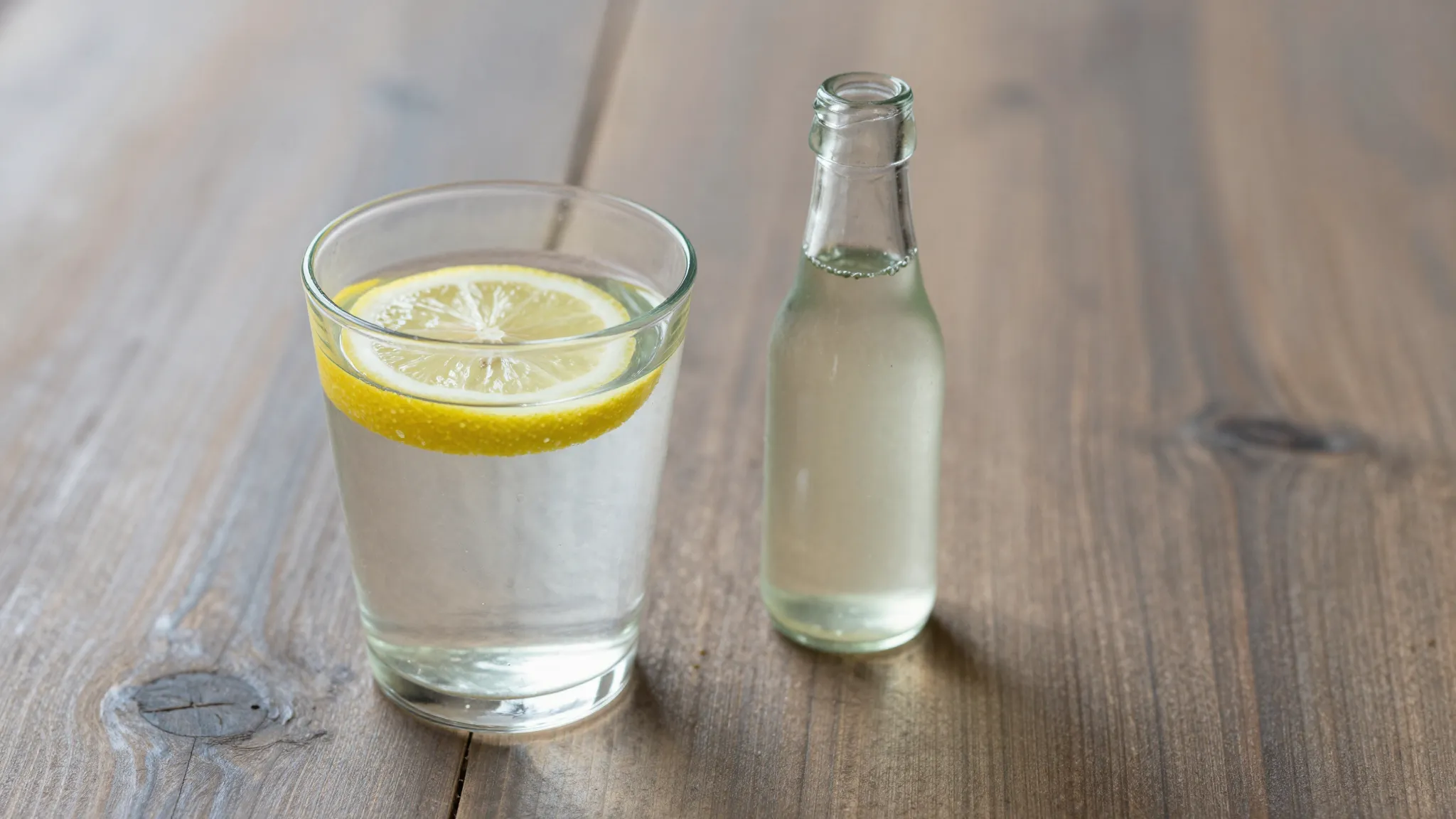 A glass of warm water with a lemon slice and a small bottle ...
