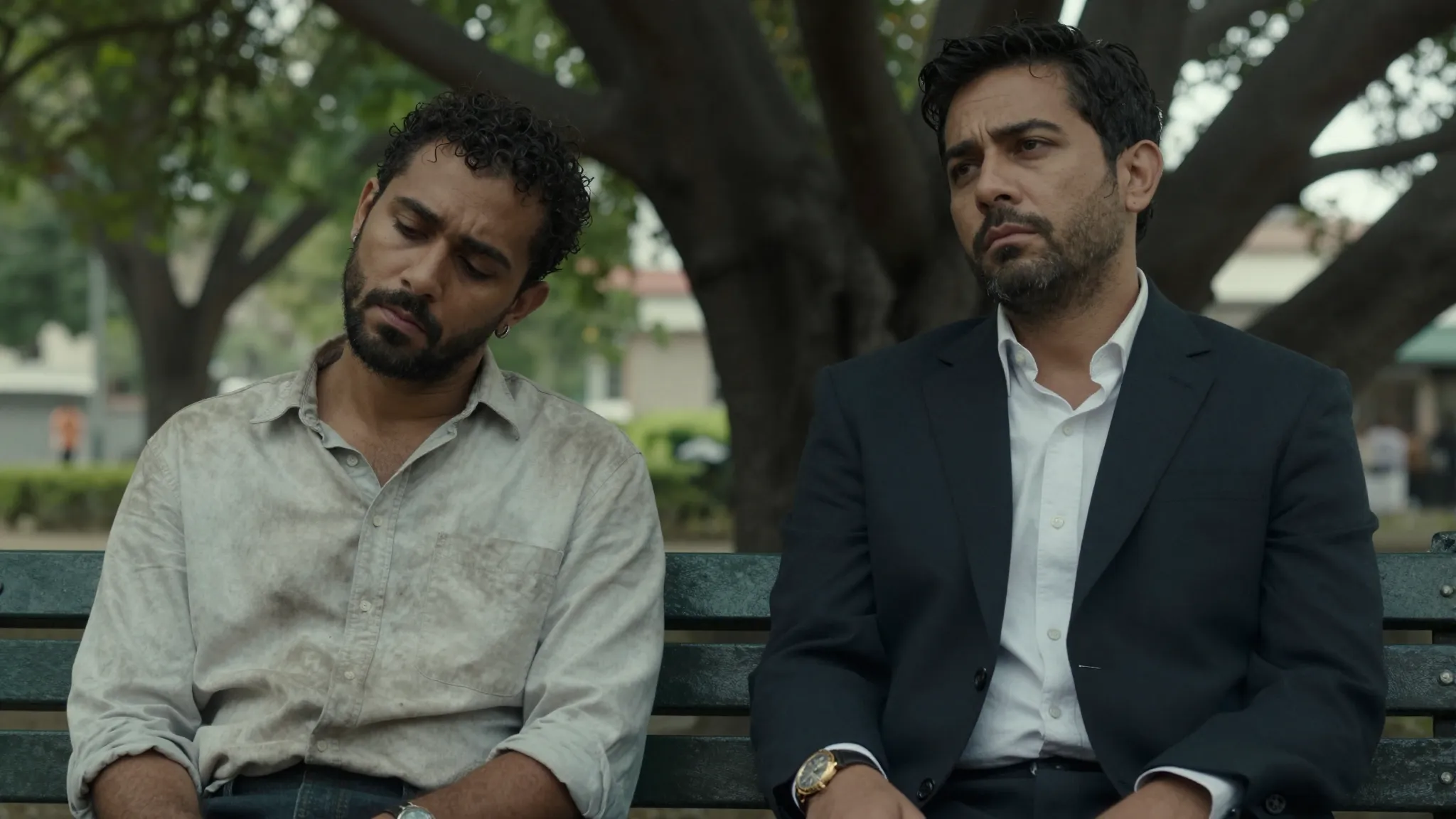 A cinematic close-up of two men sitting on a park bench unde...