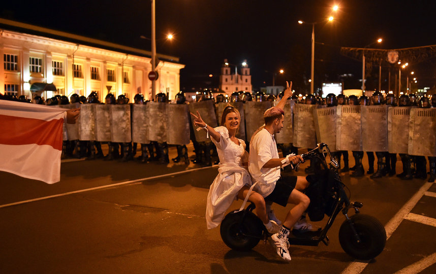 Молодожёны на скутере показывают знак мира протестующим и силовикам. Фото AFP