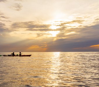 Два каякера плывут на каяке по черному морю вдоль берега  на фоне прекрасного заката.  Побережье Крыма.